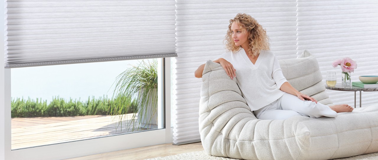 Women lounging in a chair next to large windows featuring Duette® Honeycomb Shades.